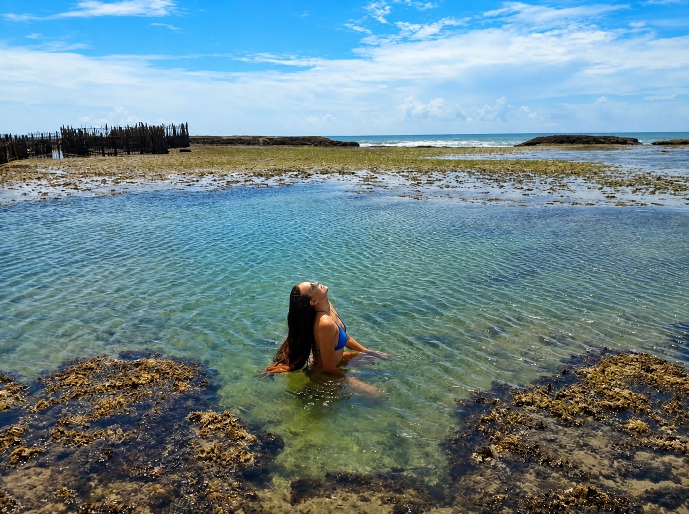 Banhista sentada dentro de uma piscina natural de Paracuru com o mar ao fundo